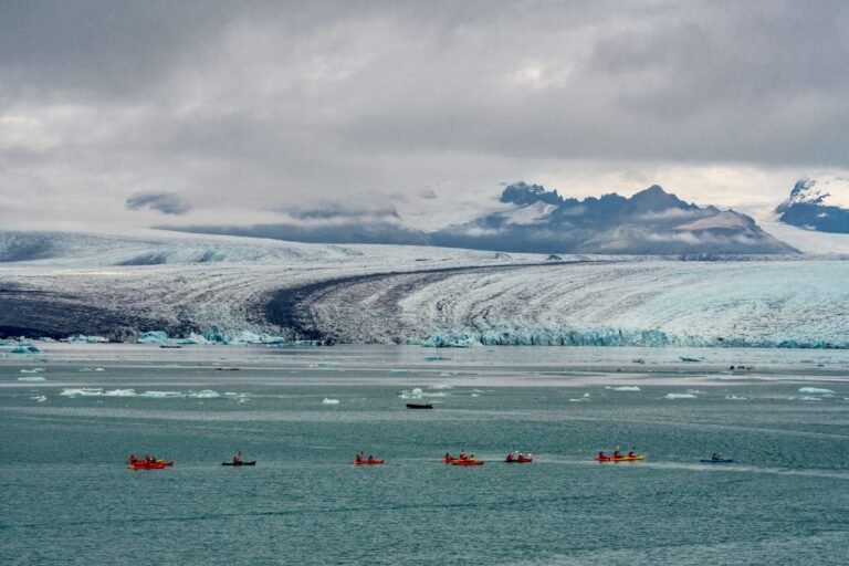 Colorful kayakers paddle near a majestic glacier in Iceland, under a dramatic sky.