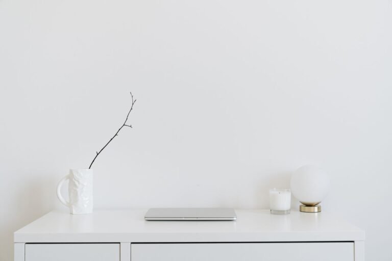 A clean, minimalistic workspace featuring a white desk, laptop, and decorative items, perfect for modern design inspiration.